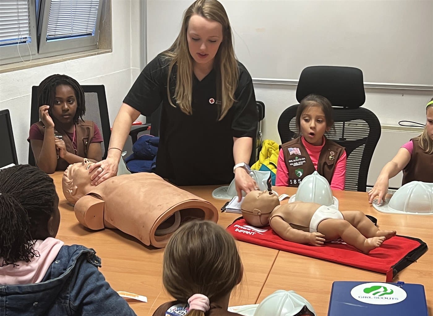 A Red Cross professional showing Girl Scouts how to give CPR using practice mannequins